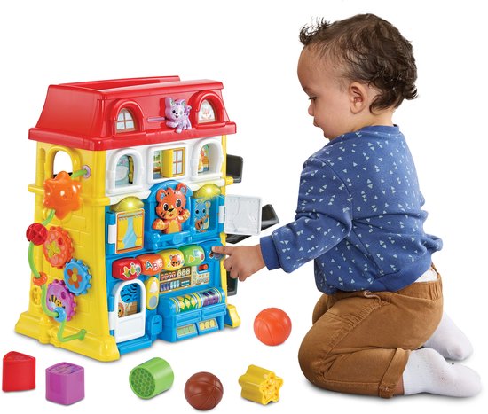 Baby speelt met geel speelhuis met rode dak, speelgoedblokken en ballen.