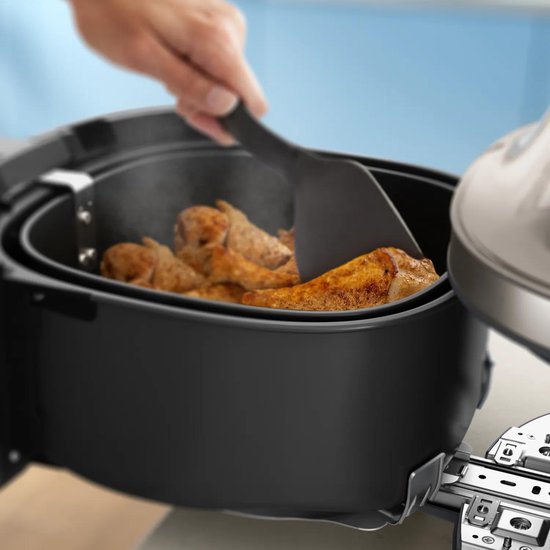 Een hand met een spatel keert goudbruine kipdelen om in een zwarte Philips Airfryer. Rook komt uit de kuip.
