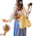 Vrouw in blauwe jurk met gele tas, houdt een herfstboeket en een esdoornblad vast. Ze heeft een camera.
