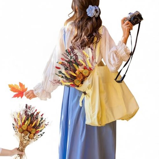 Vrouw in blauwe jurk met gele tas, houdt een herfstboeket en een esdoornblad vast. Ze heeft een camera.