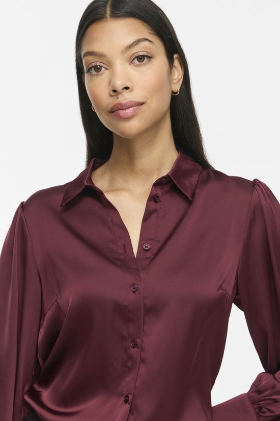 Close-up van model in bordeauxrode satijnen blouse met lange pofmouwen en knoopsluiting.