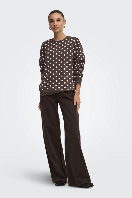 Model draagt een bruine sweater met witte polkadots, gecombineerd met een bruine broek.