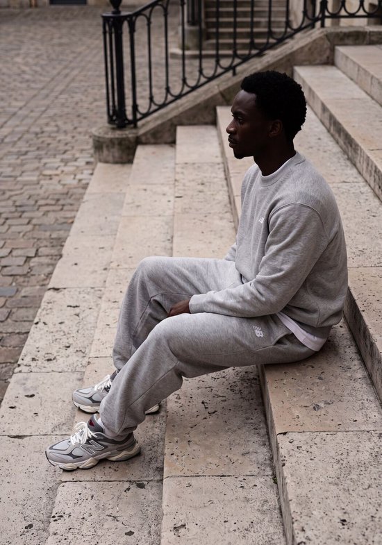 Man zittend op een trap in een grijze New Balance sweater.
