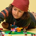 Jongen met rode muts bouwt aan kleurrijke LEGO creaties op een groene bouwplaat.