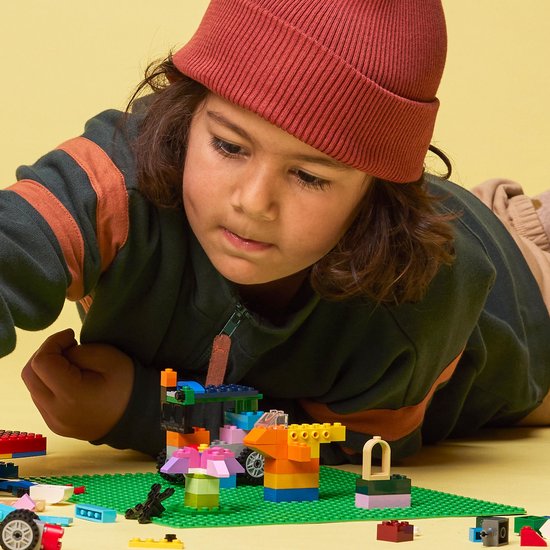 Jongen met rode muts bouwt aan kleurrijke LEGO creaties op een groene bouwplaat.