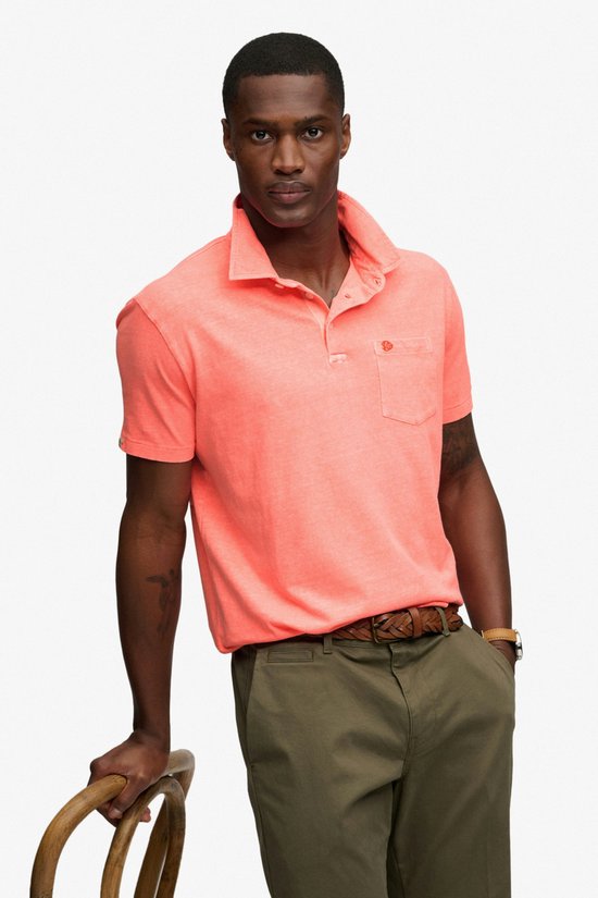 Man leunt op stoel met oranje poloshirt, olijfgroene broek en bruine riem.