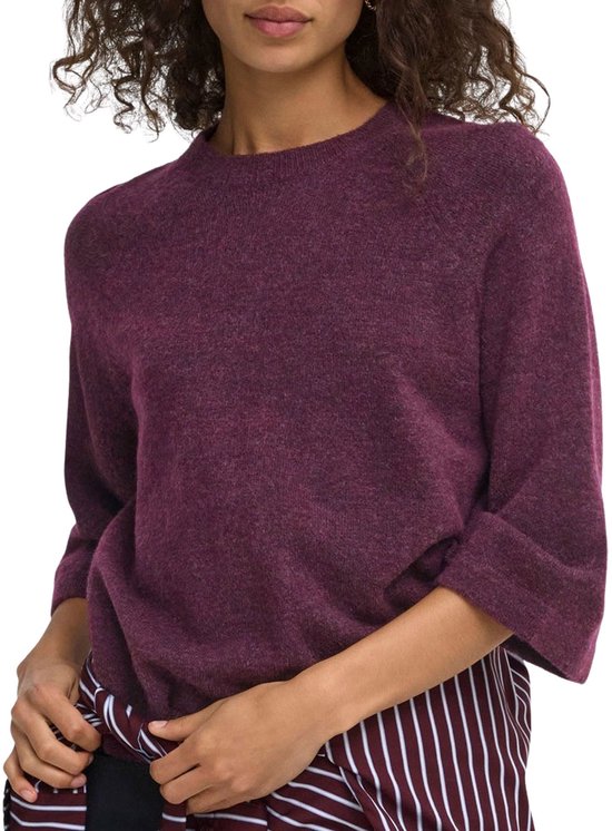 Een vrouw draagt een bordeauxrode trui met driekwartmouwen over een gestreepte blouse.
