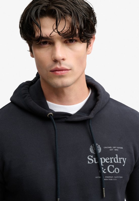 Portret van man in donkerblauwe hoodie met 'Superdry & Co' logo.
