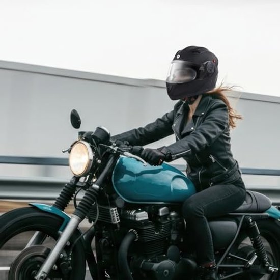 Vrouw met zwarte systeemhelm op een blauwe motorfiets, rijdend op een weg.