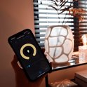 Een hand houdt een smartphone vast met de Calex-app, gericht op een glazen tafellamp met gloeidraad.