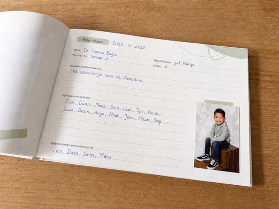 Een jongen in een lichtgrijze hoodie en spijkerbroek zit op een houten kistje, lachend naar de camera.