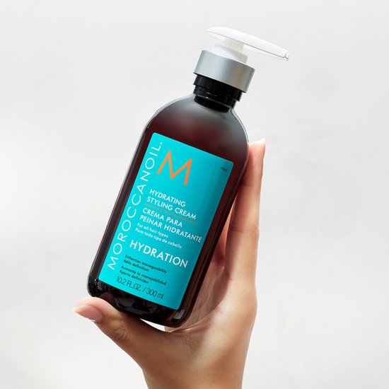 Bruine fles met pompdispenser van Moroccanoil Hydrating Styling Cream. Turquoise label met oranje M-logo.