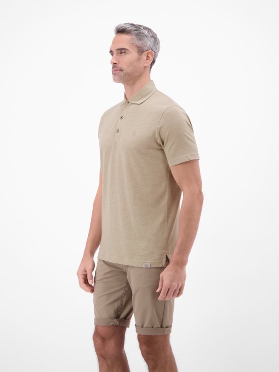 Man staand in een lichtbruin gemêleerd poloshirt en een beige short.