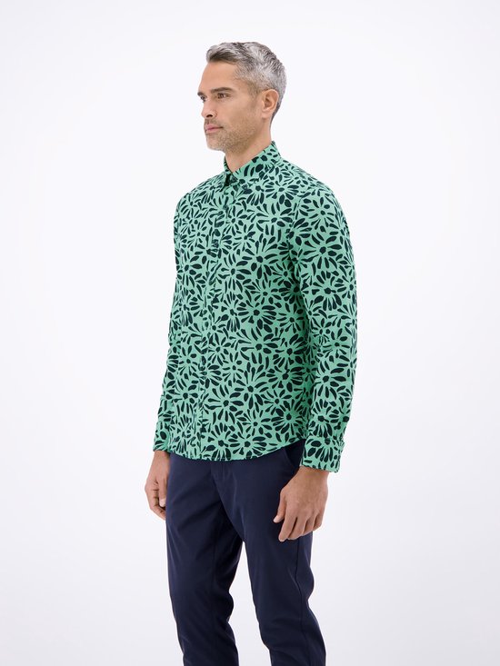 Man met grijs haar, gekleed in een mintgroen overhemd met donkerblauwe bloemenprint en marineblauwe broek.
