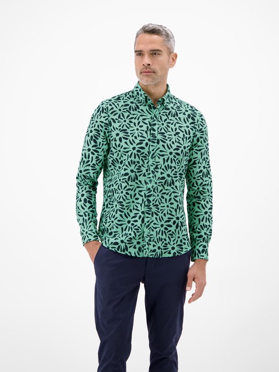 Man met grijs haar, gekleed in een mintgroen overhemd met donkerblauwe bloemenprint en marineblauwe broek.