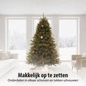 Een groene kunstkerstboom met lichtslingers en kerstballen in een modern ingerichte woonkamer.