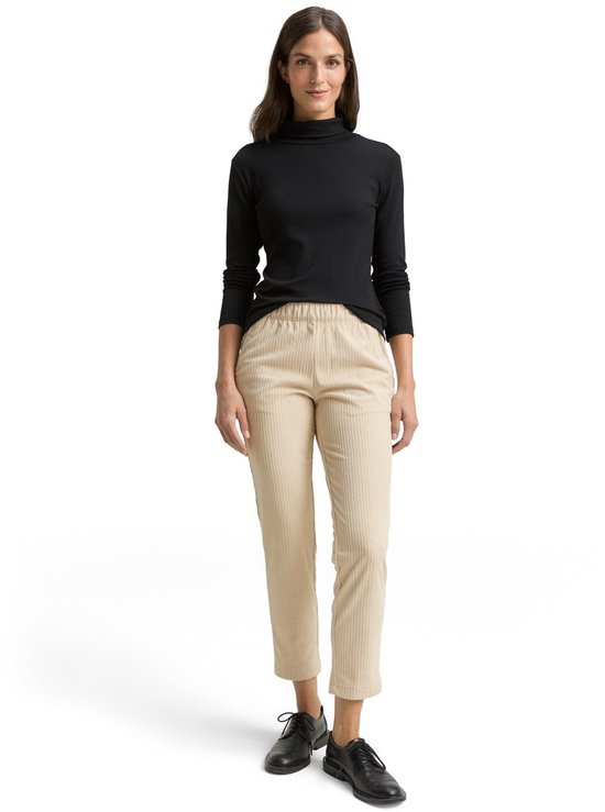 Vrouw draagt een zwarte coltrui en een beige corduroy broek.