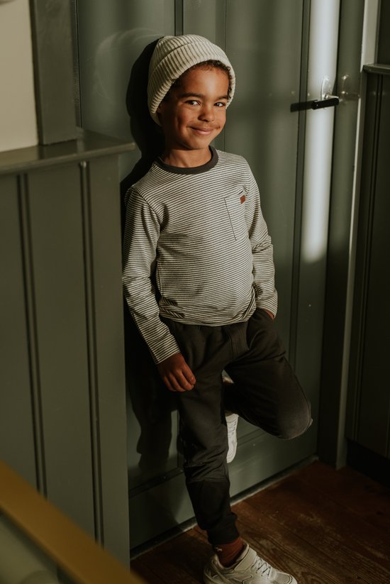Jongen draagt een lichtgrijs gestreept longsleeve T-shirt met een borstzak en een gebreide muts.