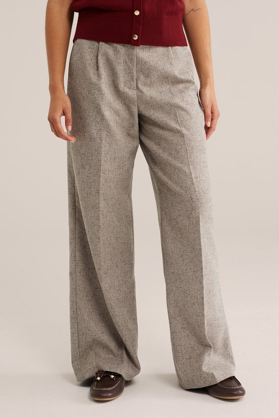 Model in een gemêleerde grijze wijde broek met persplooien.