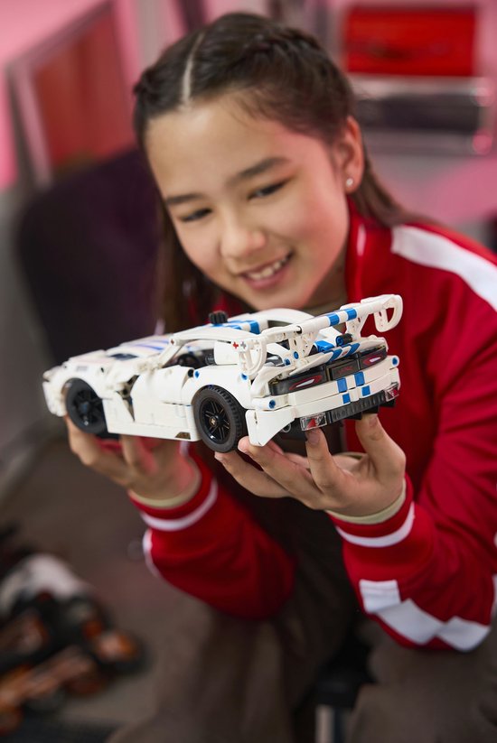 Een jong meisje met een rode jas bekijkt de achterkant van een witte LEGO Technic Dodge Viper GTS-R sportauto.