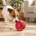 Een hond duwt met zijn neus tegen een rode bal met poot- en botafdrukken.