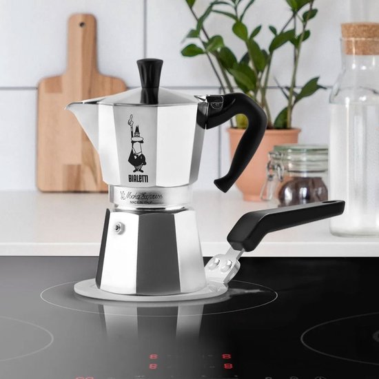 Zilverkleurige Bialetti inductie-adapterplaat met zwart handvat, geplaatst op een inductiekookplaat.