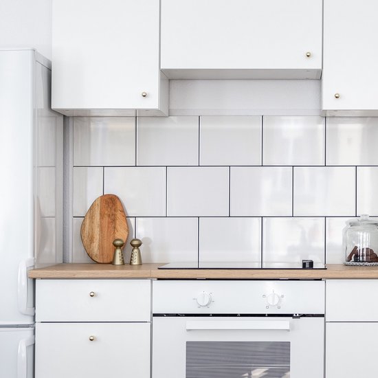 Cuisine blanche avec un plan de travail en bois, des carreaux blancs, un four blanc et des salières-poivrières.
