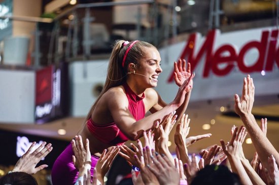 Een sportieve vrouw met een staartje en hoofdband geeft high-fives aan een publiek.