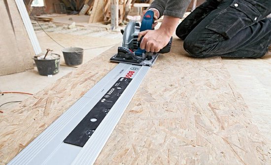 Man op knieën gebruikt een Bosch cirkelzaag op een geleiderail op een houten ondergrond.