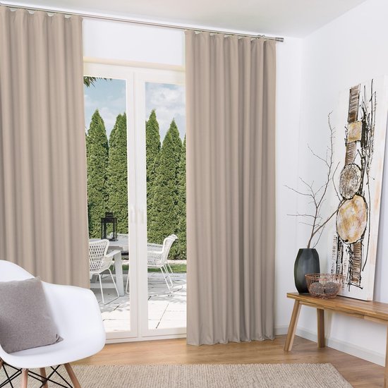 Twee beige gordijnen in een woonkamer met uitzicht op een tuin, naast een witte stoel.