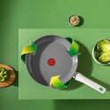 Grijze koekenpan met witte handgreep, omringd door groene recycle-pijlen. Naast de pan liggen sla en een paprika.