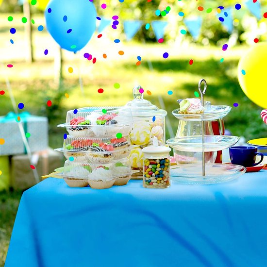 Een buitentafel gedekt met een blauw tafelkleed, versierd voor een feestje met taarten, snoep en ballonnen.