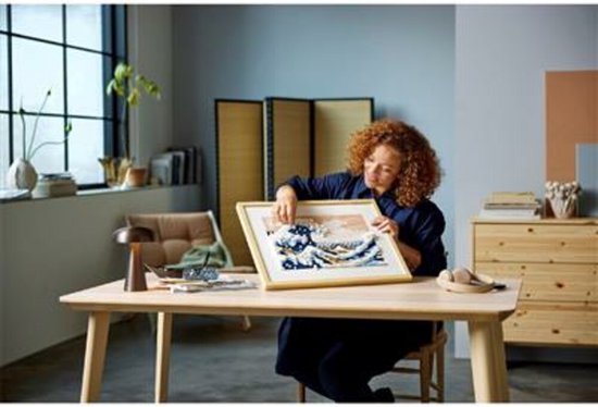 Une femme aux cheveux bouclés construit une mosaïque LEGO Art Hokusai - La Grande Vague.