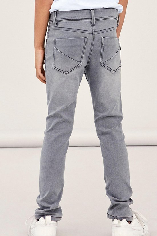 Achterkant van een grijze, aansluitende jeans met opgestikte achterzakken en zwarte stiksels.