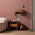 Zwarte vogelmuurdecoratie op een roze muur boven een houten nachtkastje.