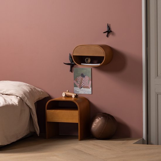 Zwarte vogelmuurdecoratie op een roze muur boven een houten nachtkastje.