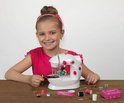 Meisje met een roze strik in het haar, zittend voor een witte kindernaaimachine met roze details.