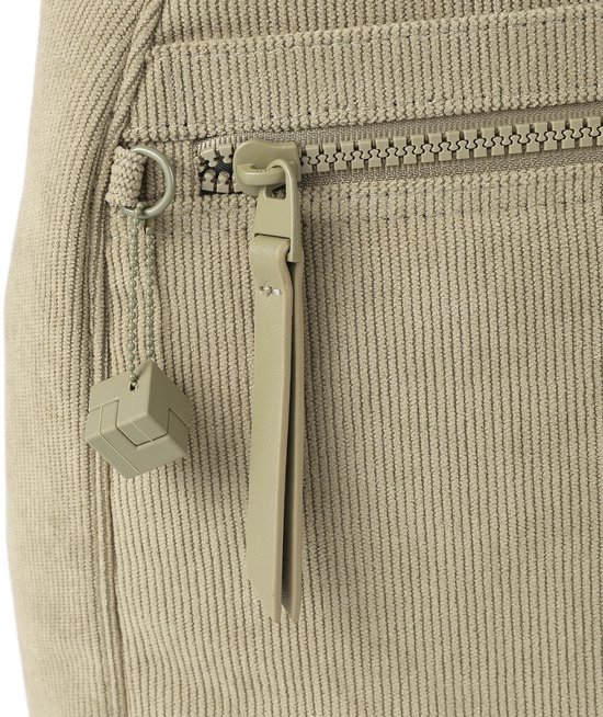 Detail van de beige ribfluwelen rugzak: rits, ritstrekker, en een kubusvormig hangertje.