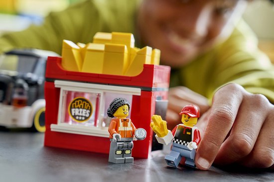 LEGO poppetjes bij frietkraam. Serveerster met rode pet geeft frietjes aan klant met oranje vest.