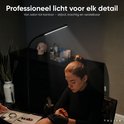 Een tatoeëerder werkt aan een pols, verlicht door een zwarte TULITE Arcus Vloerlamp.
