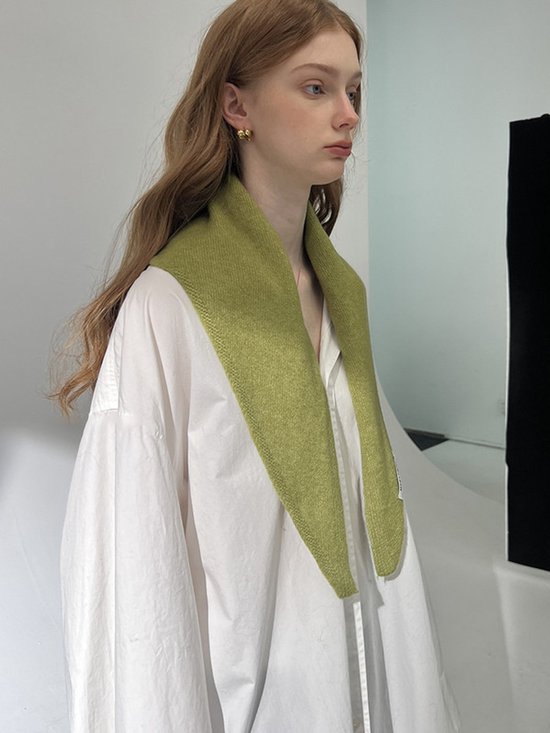 Close-up van een model met een wit overhemd en een olijfgroene sjaal die als kraag gedragen wordt.