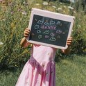 Kind met roze jurk houdt roze lichttablet met 'JEANNE' en hartjes vast in de wei.