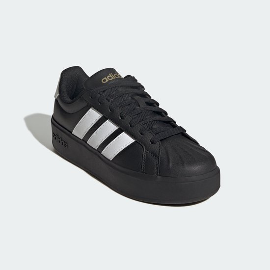Zwarte damessneaker met witte Adidas-strepen, platformzool en gouden logo op de tong.
