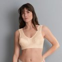 Vrouw in nude beha zonder beugel, met kanten details, staat voor grijze achtergrond.