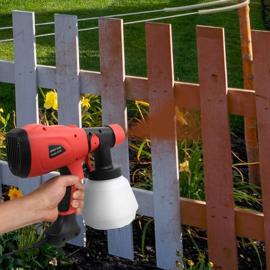 Hand met rode verfspuit spuit oranje verf op een witte houten schutting.
