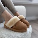 Cognacbruine suède pantoffels met dikke crèmekleurige bontvoering, gedragen door een model.