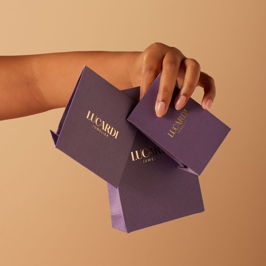 Main à la peau brune tenant trois boîtes cadeaux violettes Lucardi Juwelier.