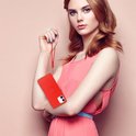 Vrouw met lange rode haren in een roze jurk, houdt een lichtrode telefoonhoes met ring vast.