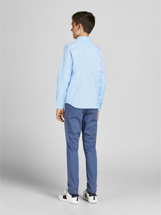 Un garçon porte une chemise bleu clair à manches longues et un pantalon bleu.