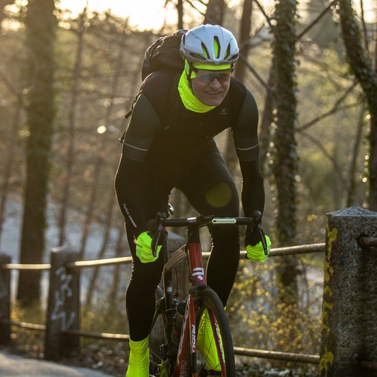 Een fietser in het schemerdonker draagt een helm en opvallende fluorgele handschoenen en beenstukken.